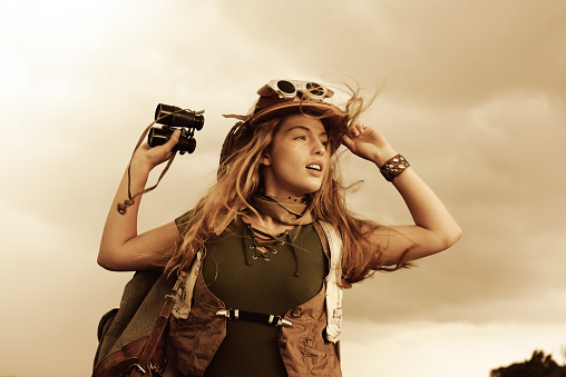 A young girl dresses up as an explorer. She wears a
jungle hat and holds a binocular in her hand. The 
wind passes through her hair as she observes the 
area.