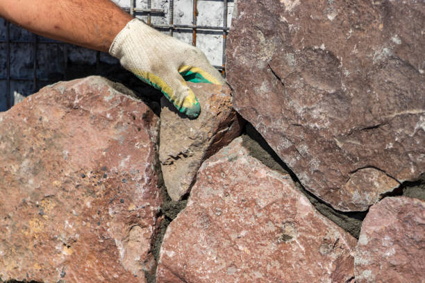 istock Builder - mason hands placing stones on a wall using cement, outdoors 1187006240