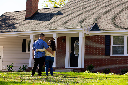 Young couple in front of new home hugging