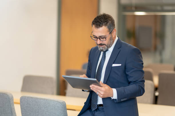 istock A smart-suited, bespectacled and saccid boss who controls both instant data and social media using his tablet as he wanders through the office 1187014574