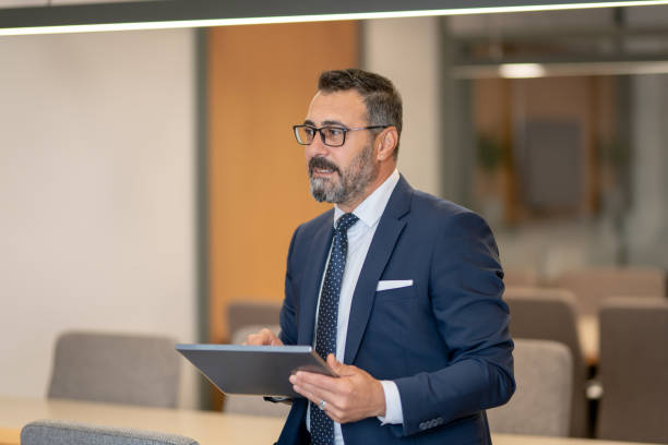 istock A smart-suited, bespectacled and saccid boss who controls both instant data and social media using his tablet as he wanders through the office 1187014619