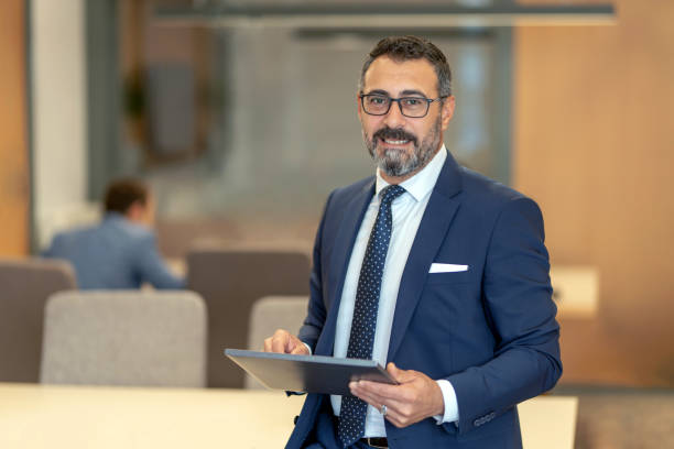 istock A smart-suited, bespectacled and saccid boss who controls both instant data and social media using his tablet as he wanders through the office 1187015637