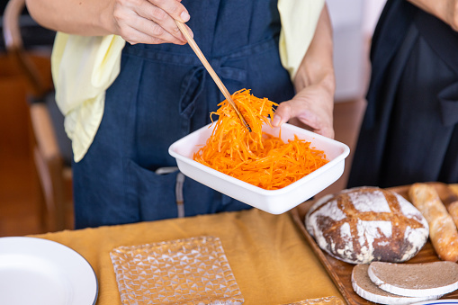 Women putting sliced carrot to dish for lunch party