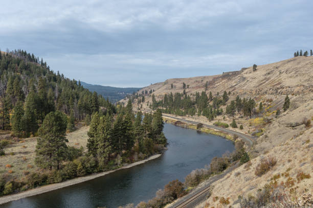 istock Curved river and train tracks cutting through valley tree lined hills 1187019707