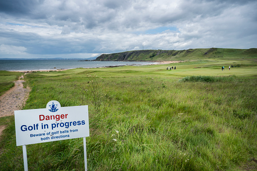 Earlsferry, Scotland, UK - June 17, 2019: A sign warns hikers about the danger of getting hit with a golf ball while approaching scenic West Bay, a sandy stretch of coastline curving from Kincraig Point to Earlsferry along the Fife Coastal Path, a 117 mile hiking trail on the eastern coast of Scotland, Fife.