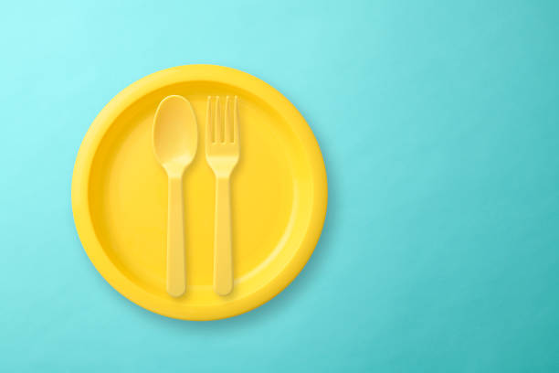 Overhead shot of yellow plastic plate with Folk and spoon on light blue background with copy space.