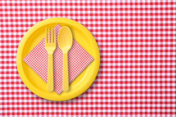 istock Yellow plastic plate with folk and spoon on red gingham check tablecloth 1187037758