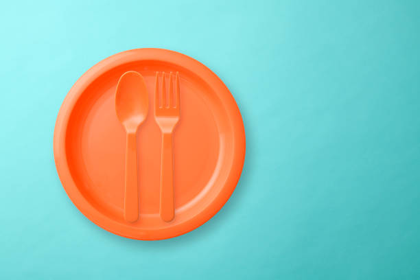 Overhead shot of orange color plastic plate with Folk and spoon on light blue background with copy space.