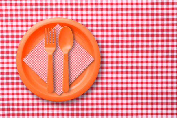 istock Orange color plastic plate with folk and spoon on red gingham check tablecloth 1187037767