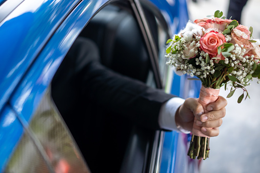 Asian man hand holding flower bouquet out from bridal car