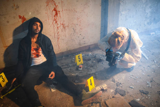 Forensic Scientist Photographing Evidence at Crime Scene Elevated view of African male murder victim leaning against blood-splattered wall and Caucasian female forensic scientist photographing evidence. dead person photos stock pictures, royalty-free photos & images