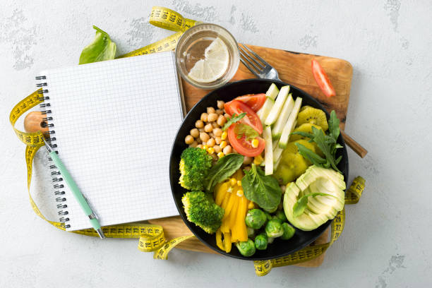 비건 건강한 균형 잡힌 식단 빈 노트북과 측정 테이프채식 불상 그릇. 히피아, 브로콜리, 후추, 토마토, 시금치, 아루굴라, 아보카도를 흰색 배경에 접시에 얹어 놓습니다. 맨 위 보기 - weight loss 뉴스 사진 이미지