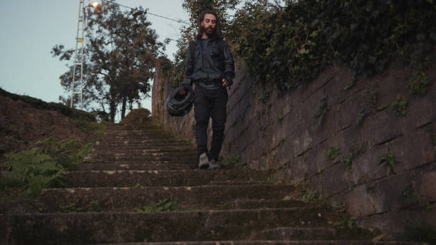 istock Young handsome biker with long hair is going down through stairs with motorcycle helmet on his hand 1187079784