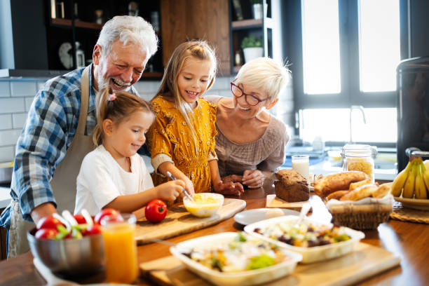 felice coppia senior che sta facendo colazione con i loro nipoti a casa - grandparent grandfather grandmother child foto e immagini stock