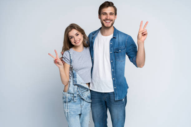 smiling young casual couple making victory or peace sign on white background. smiling young casual couple making victory or peace sign on white background peace sign gesture photos stock pictures, royalty-free photos & images
