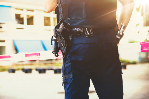 Policeman on on a crime scene investigation Policeman on crime scene . Red plastic tape and police officer, gun belt, handcuffs and gun.With a sunshine flare coming in. weapon stock pictures, royalty-free photos & images