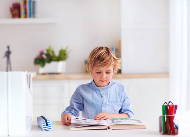 istock young kid, boy reading a book while sitting at the desk at home 1187089618