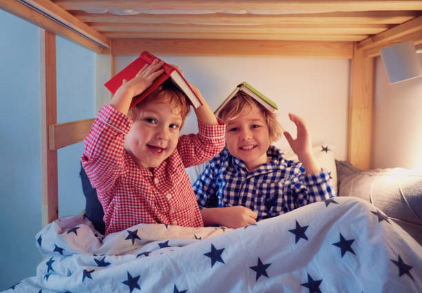 cheerful kids, brothers having fun, playing with books on the bunk bed during bedtime cheerful kids, brothers having fun, playing with books on the bunk bed during bedtime baby sleeping bedding bed stock pictures, royalty-free photos & images