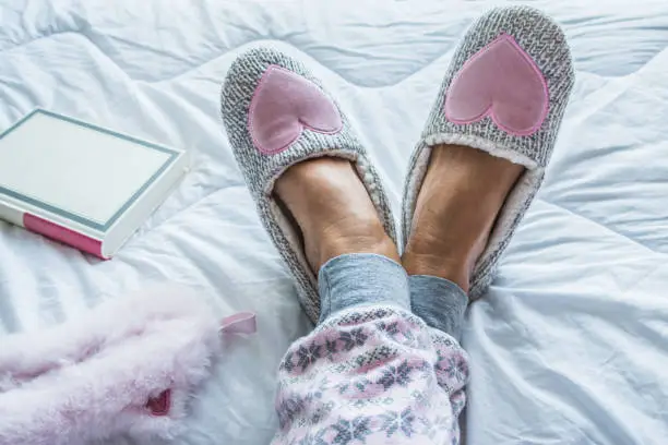Close Up of Senior Woman Legs in Fluffy Slippers on the Bed