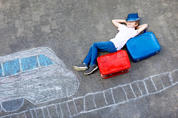 istock Little kid boy having fun with fast train picture drawing with colorful chalks on asphalt. Child painting with chalk and crayon and going on vacations. Schoolkid sitting on suitcase. 1187093369