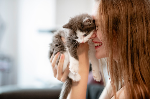 Woman holding up a kitten and smiling, cuddling her.