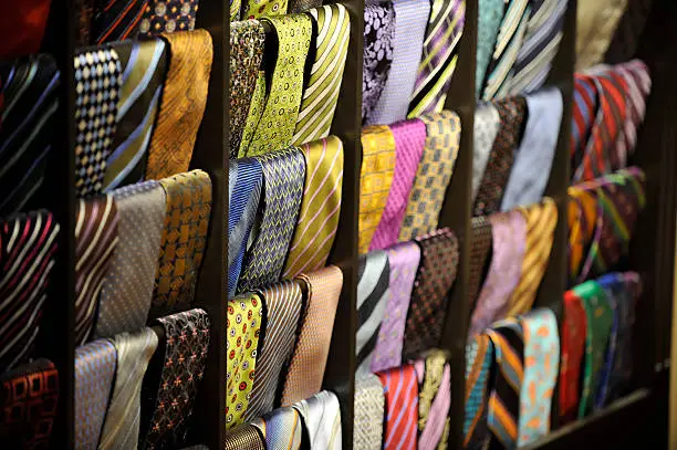 Colorful display of dozens of men's ties hanging on a wooden display rack, photographed with a very shallow depth of focus.