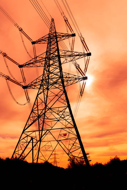 istock Silhouette of high voltage cables and electricity pylons set against a digitally generated orange coloured sunset sky in England. 1187112103