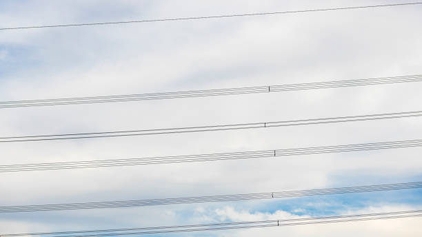 Close up of parallel rows of high voltage electricity cables silhouetted against clouds in the sky.