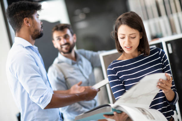 istock A young woman reading form a large catalog while a salesman is having a conversation with a man behind her in the store 1187116251