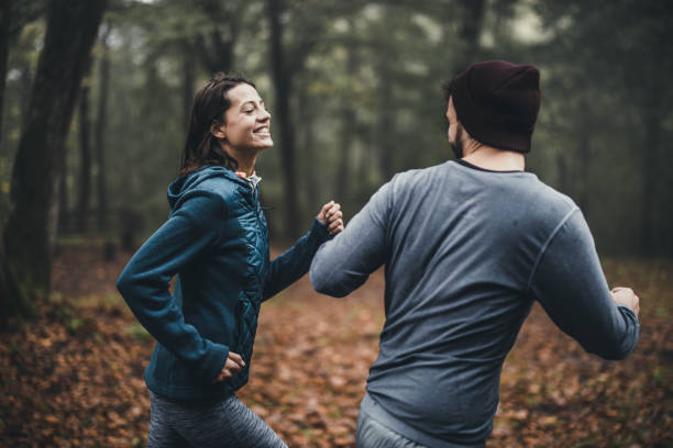 giovane coppia atletica felice che si diverte mentre fa jogging nella giornata autunnale all'aperto. - jogging autumn young women women foto e immagini stock
