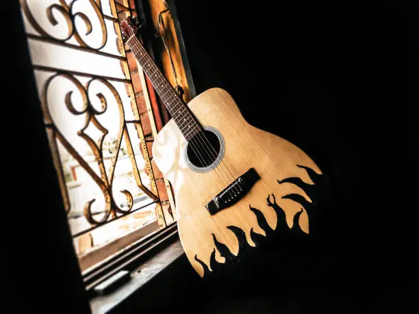 An acoustic guitar placed next to the old vintage window with soft sunlight coming from. Nostalgia guitar chords. Summer melody background. Close up.