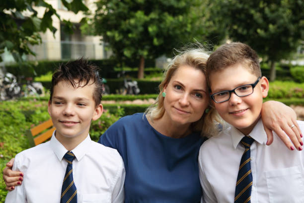 Two cheerful teenage boys in their formal wear / uniforms are standing and posing for a family portrait with their mother stock photo