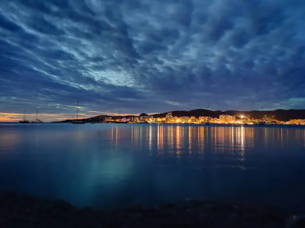 City lights reflect in the water at dusk on Ibiza island
