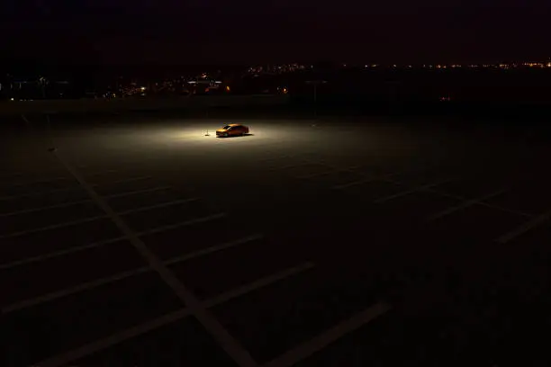 Photo of A single car in a parking lot representing the concept of working late