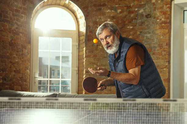 Senior man playing table tennis in workplace, having fun