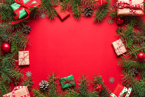 istock Christmas flat lay frame made of fir branches, gift boxes, red holiday decorations on red background 1187132879