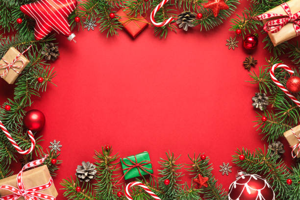 istock Christmas frame made of fir branches, gift boxes, red holiday decorations and candy on red background 1187132919