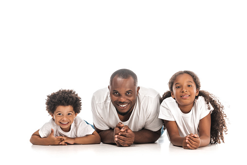 happy african american father, son and daughter smiling at camera while lying on white background