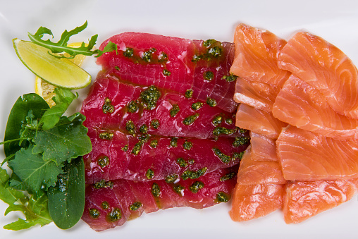 Mixed sliced fish: salmon and tuna decorated with greens and lemon in white plate
