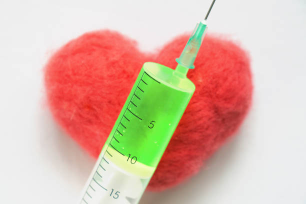 Syringe with a green medicine lying on a red heart which lying on the white bed sheet. Heart treatment concept