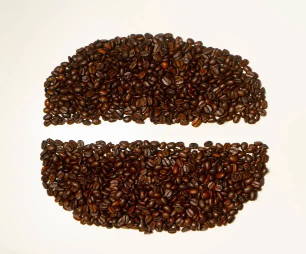 Coffee beans in the shape of coffee bean on the white wooden table. Separate coffee beans. Food and drink background or texture.
