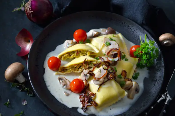 Swabian vegetable ravioli (so called 'Maultaschen') with mushroom cream sauce and roasted onion rings, dark and moody style