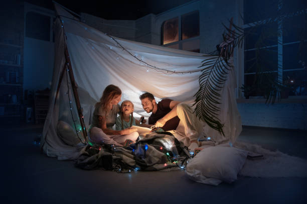 istock Family sitting in a teepee, reading stories with the flashlight 1187143454
