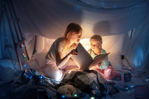 Mother and daughter sitting in a teepee, reading stories with the flashlight