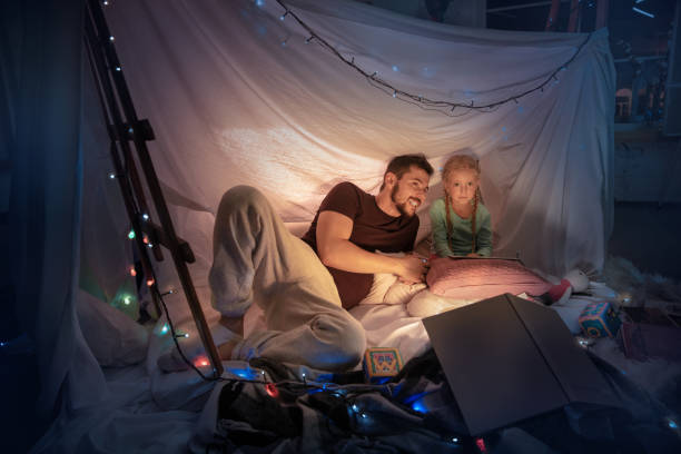 istock Father and daughter sitting in a teepee, having fun with the flashlight 1187143527