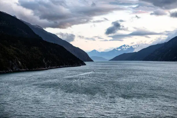 High angle view from cruise ship toward small boat motoring through Taiya Inlet and upper part of Lynn Canal near Skagway in early evening.
