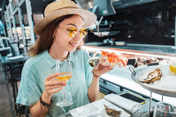 Asian woman tasting fresh raw oyster shellfish and drinking wine in seafood restaurant Asian woman tasting fresh raw oyster shellfish and drinking wine in seafood restaurant oyster photos stock pictures, royalty-free photos & images