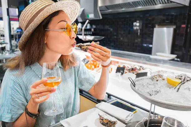 Asian woman tasting fresh raw oyster shellfish and drinking wine in seafood restaurant