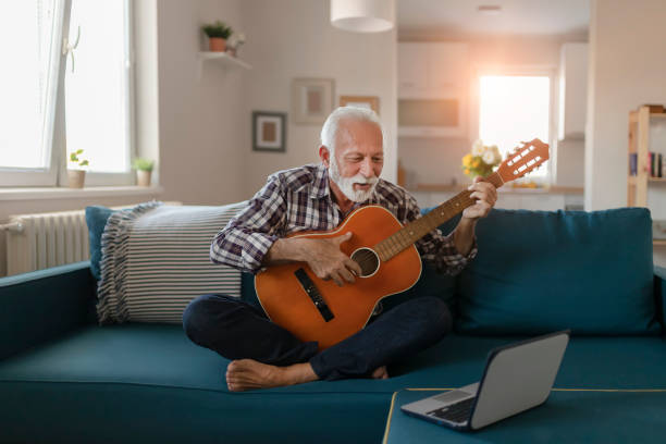 senior man apprend à jouer de la guitare acoustique en ligne - senior adult independence lifestyles home interior photos et images de collection