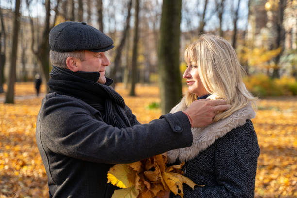 bel uomo bruna di mezza età regola con cura i suoi capelli. donna matura bionda felice. coppia amorevole di 45-50 anni camminano nel parco, si guardano l'un l'altro - 40 45 years immagine foto e immagini stock